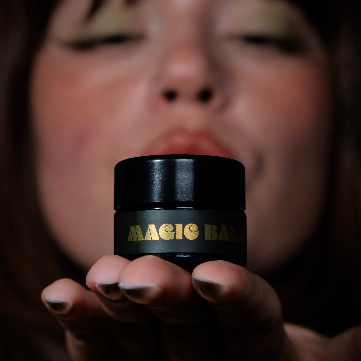 Hand holding Magic Balm jar, highlighting product packaging against dark background