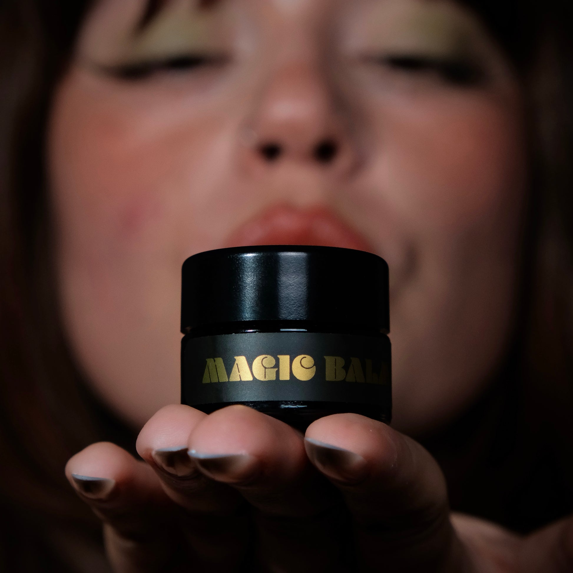 Hand holding Magic Balm jar, highlighting product packaging against dark background