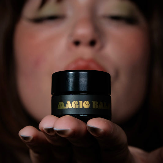 Hand holding Magic Balm jar, highlighting product packaging against dark background